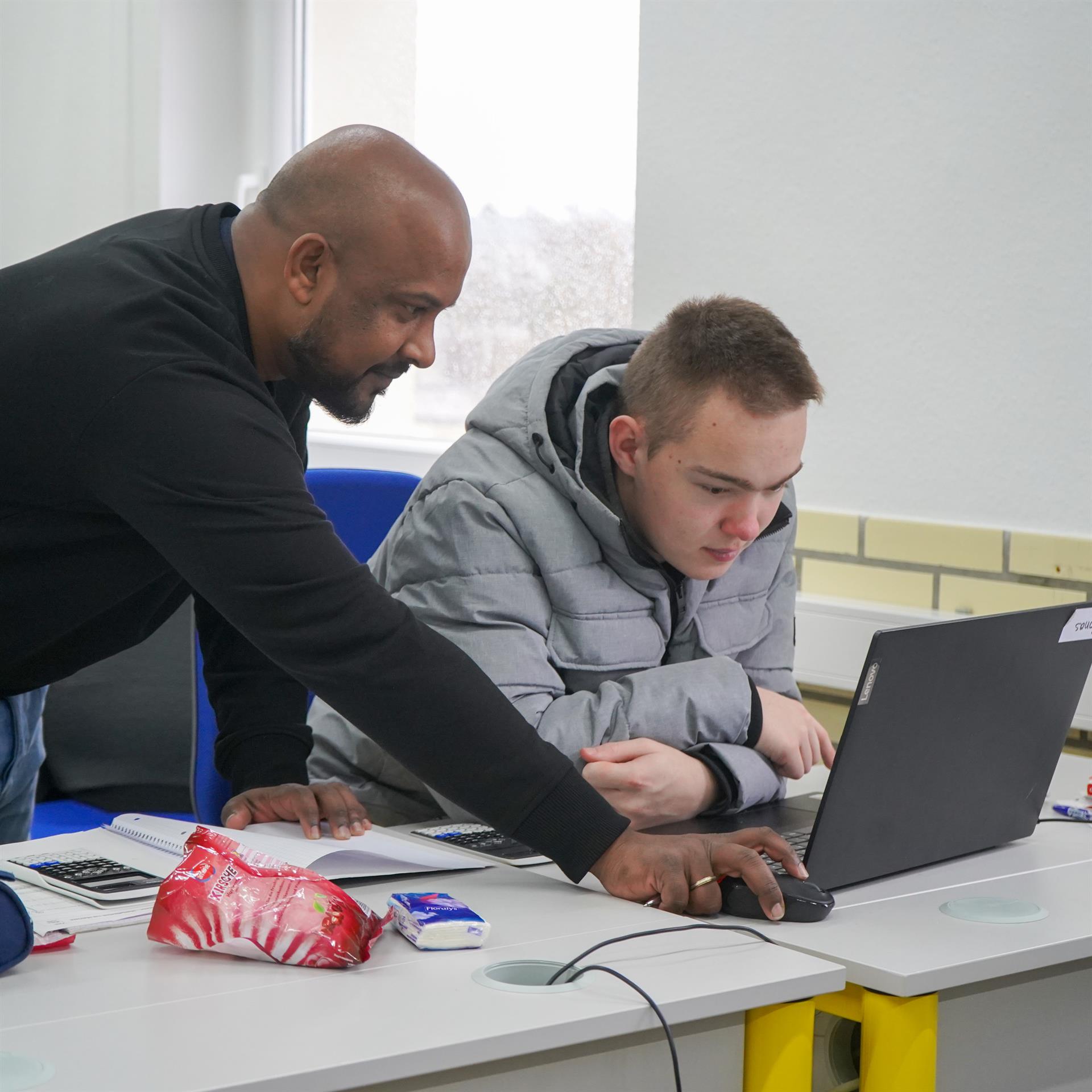 Ein Lehrer hilft einem Schüler am Laptop
